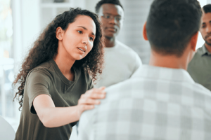 woman touches the shoulder of another group member in her alcohol detox treatment program group therapy session to console him