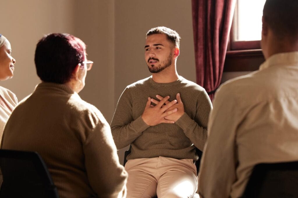 Drug Detox Center PPC 4 | Virtue Recovery Houston man holds his hands to his chest while expressing his thoughts in a group therapy session