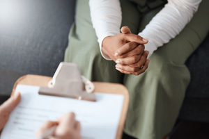 a person has their hands pressed together while a medical professional takes notes on a clipboard during a medical detox treatment program assessment