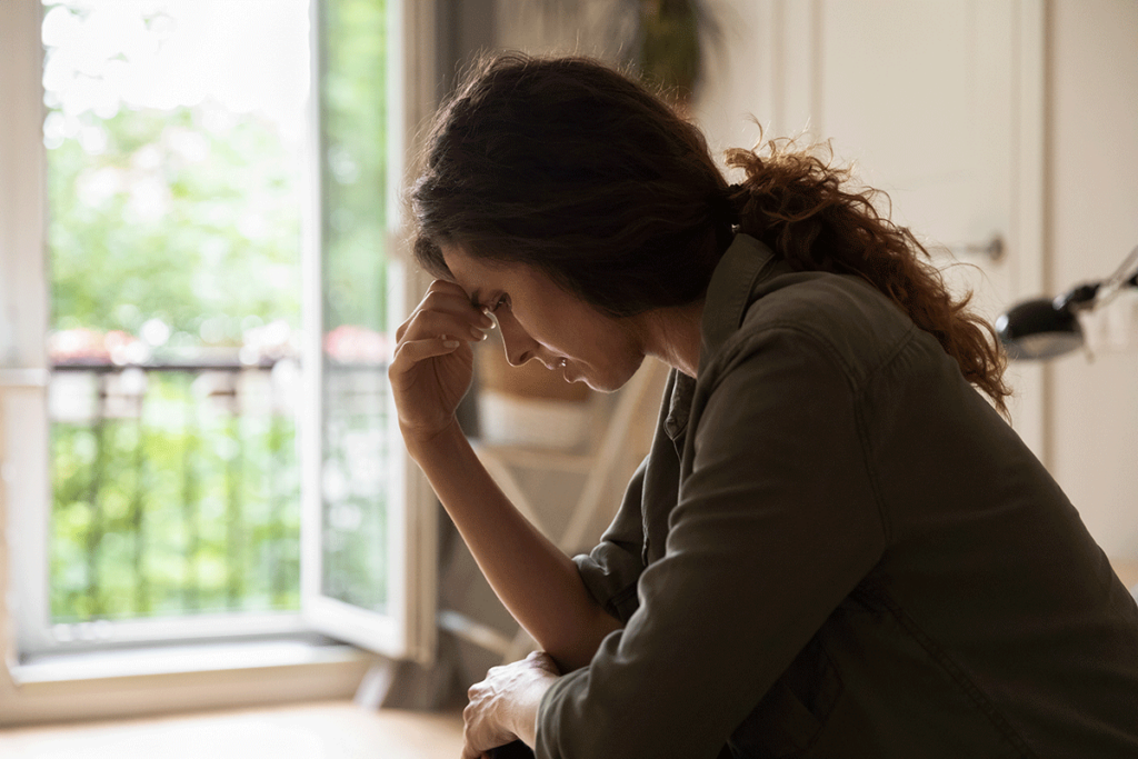 a woman sits at her desk appearing distraught and holds her hand to her forehead experiencing side effects of benzos