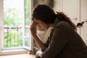 a woman sits at her desk appearing distraught and holds her hand to her forehead experiencing side effects of benzos